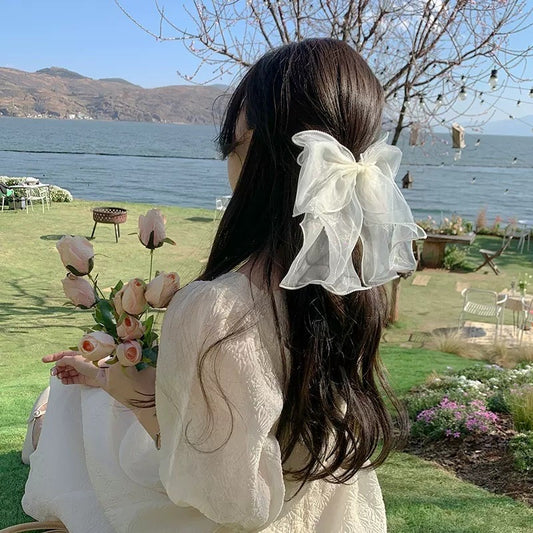 Woman with a large white bow in her hair holding flowers by a lakeside.